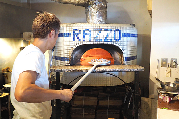 白いタイルが貼られた窯でピザを焼く様子