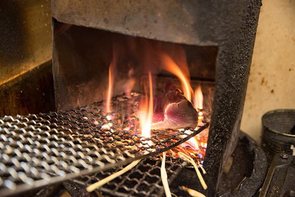 網の上で炎をあげて焼けるカツオ